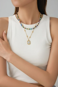 Detail of layered gold chain with colorful cylinder beads and a textured rectangular pendant