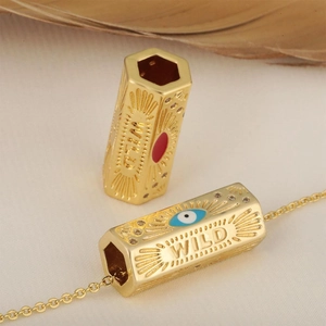 Gold-plated hexagonal evil eye charm bead with WILD engraving on a beige fabric background