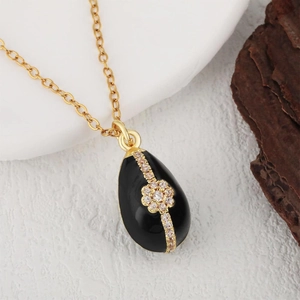Water-drop black onyx pendant necklace with gold floral zircon inlay on a white plate