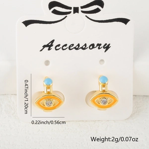 Detail of evil eye huggie earrings with orange enamel and cubic zirconia on card