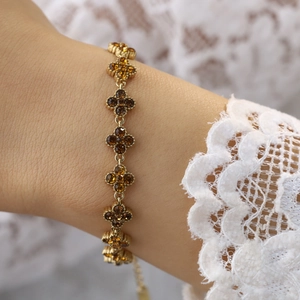 Nahaufnahme des goldenen Kleeblatt-Armbands mit orangen Kristallen auf Spitze