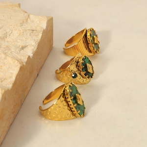 Detail van drie 18k vergulde titanium ringen met groene stenen en een gehamerde textuur