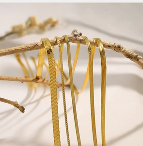Detailed view of layered gold herringbone and snake chain necklaces on a branch
