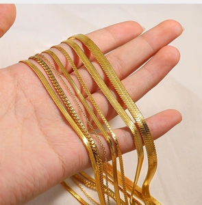 Detail of layered gold snake chains and cuban link necklaces held in hand