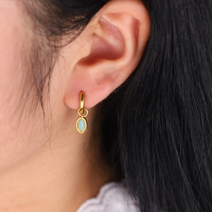 Gros plan de boucles d'oreilles créoles dorées avec pendentif pierre bleu ciel