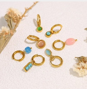 Détail de créoles dorées 18 carats avec pendentifs en pierres naturelles sur fond blanc texturé