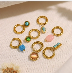 Détail de boucles d'oreilles dorées 18 carats avec pierres naturelles sur lin beige