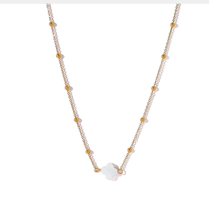 Detail van een gelaagde gouden kralenketting met een witte parelmoer klaver hanger