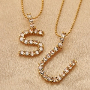 Dettaglio macro dei ciondoli S e U in oro 18K con cristalli incastonati su seta satin