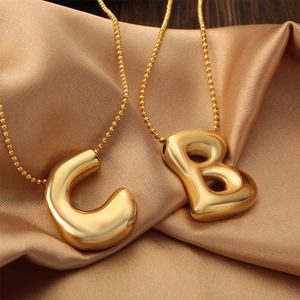 Gold puffed alphabet pendant necklaces with mirror finish on champagne silk background