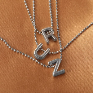Polished silver alphabet pendant necklace with spherical chain on orange silk fabric