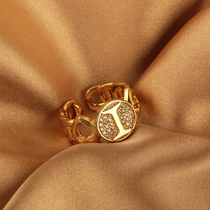 Anello dorato a catena con lettera L e zirconi incastonati su seta champagne
