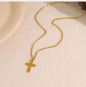 Top-down view of minimalist golden cross pendant necklace on textured beige background
