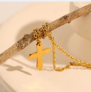Close-up of golden stainless steel cross necklace hanging on a natural wooden branch