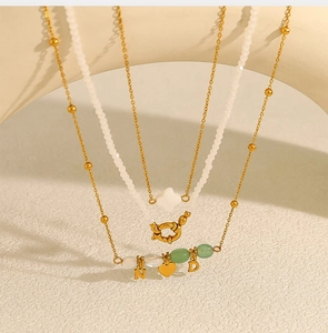 Detail van gelaagde kralenketting met hart- en letterhangers op een beige getextureerde achtergrond