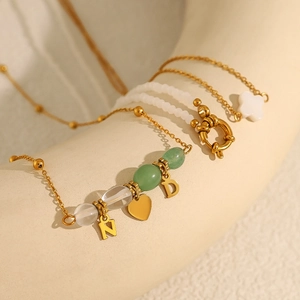Gouden ketting met hart- en letterhangers, groene kralen en klavervormige bedeltjes