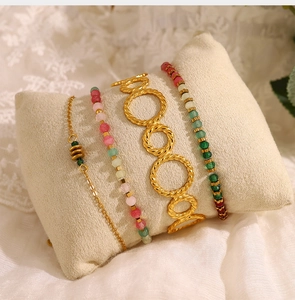 Detail of gold twisted bangle and colorful beaded bracelets on a soft velvet display cushion
