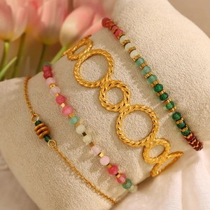 Elegant gold twisted bangle and colorful bead bracelet set on a beige jewelry pillow