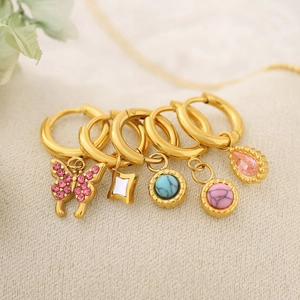 Detailed macro shot of gold huggie earrings with butterfly, star, and stone charms