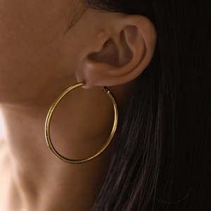 Macro shot of large gold hoop earrings with bamboo textured metal details on a model
