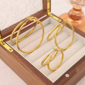 Three pairs of gold bamboo-textured hoop earrings in varied sizes on a wood tray