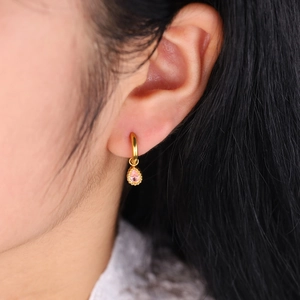 Gold-plated hoop earrings with a drop-shaped pink gemstone pendant on a female model