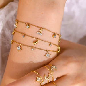 Detailopname van gouden armbanden en ringen met ster, maan en kers bedels met kristal