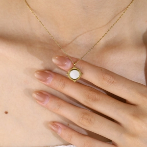 Detailed close-up of a golden round necklace featuring white shell inlay worn on the neck