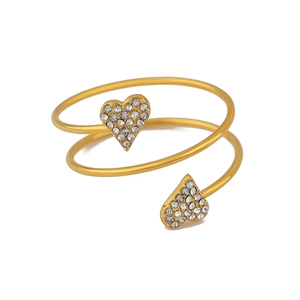 Macro-opname van gouden spiraal armband met twee hartvormige bedeltjes en zirconiazand