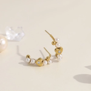 Detail van gouden C-vormige oorbellen met hartvormige hanger en witte parels