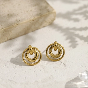 Detalle de pendientes de doble aro dorados con texturas lisas y ondas irregulares