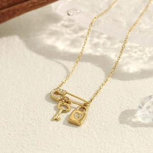 Macro detail of 18K gold necklace with micro-pave safety pin, key and lock pendants