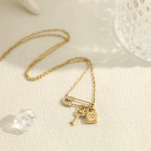 Detail of 18K gold chain featuring safety pin, key, and heart padlock charms with crystals