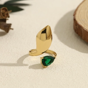 Close-up of irregular gold ring with pear-cut green zircon on textured sandy surface