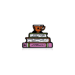 Enamel pin with orange teacup on stack of colorful books, artistic illustration style
