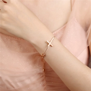 Dettaglio del bracciale in oro rosa con ciondolo a croce e cuore indossato da una modella