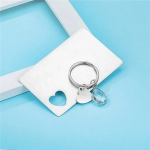 Polished heart keychain with a blue crystal drop on a decorative metal card display