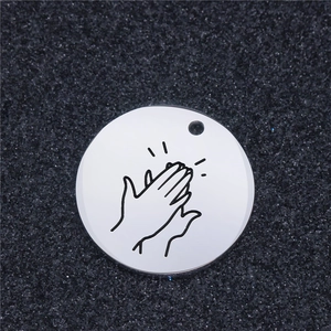 Macro view of a round stainless steel charm with a black engraved hand clapping design