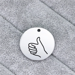 Macro detail of round stainless steel pendant with engraved thumbs-up hand gesture sign