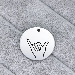Close-up of polished silver steel round tag with black engraved Shaka gesture line art
