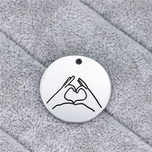 Macro detail of polished stainless steel round pendant with heart gesture engraving