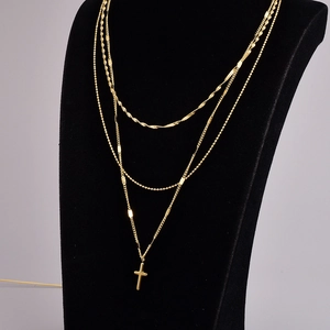 Dettaglio della collana a strati dorata con croce mostrata su un busto nero lucido