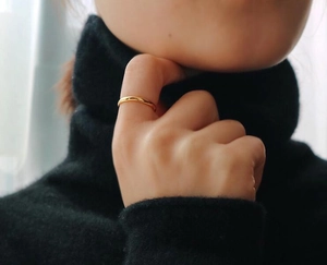 Nahaufnahme eines minimalistischen, 18K vergoldeten Rings am Finger auf dunklem Stoff
