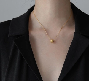 Dettaglio ravvicinato di una collana dorata con ciondolo a sfera testurizzata al collo