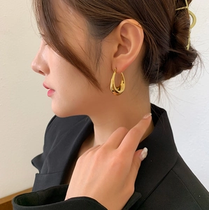 Polierte goldene Tropfenohrringe aus Titanstahl an einem Model in einem schwarzen Blazer