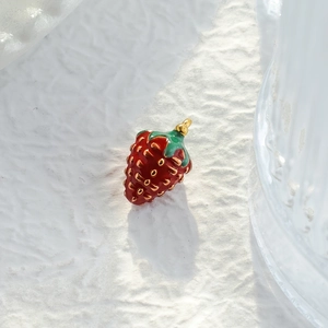 Vintage aardbei-emaille hanger in rood en goud op een witte ondergrond met textuur