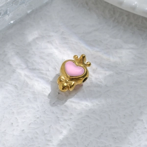 Macro shot of gold pendant with pink heart enamel, crown motif, and small bow detail