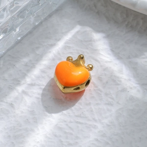 Macro detail of a 14K gold-plated heart charm with orange enamel and a crown accent