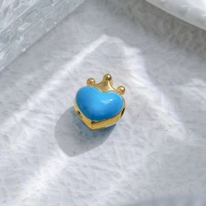 Macro detail of sky blue enamel heart charm with golden crown on white background