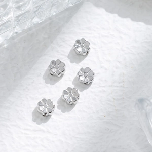Detailed close-up of five-petal silver flower beads for DIY jewelry on white stone